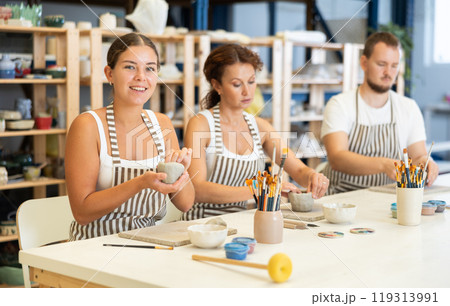 Three pottery workshop workers sculpt from raw clay 119313991
