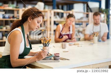 Three craftsperson are busy painting clay products Three craftsperson are busy painting clay products 119313992