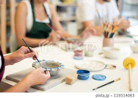 Closeup of female hands painting ceramic plate with paint and brush in pottery workshop 119314063