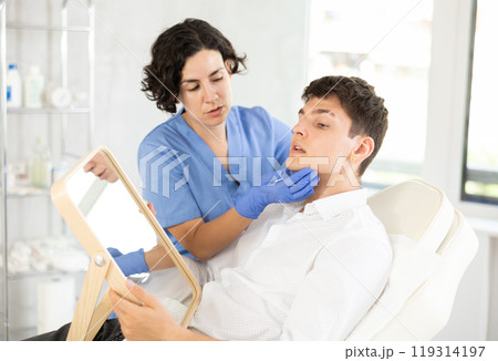 Young man having consultation about face aesthetic while looking in the mirror Young man having consultation about face aesthetic while looking in the mirror 119314197