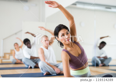 Focused asian woman practicing Hatha yoga postures with group 119314289