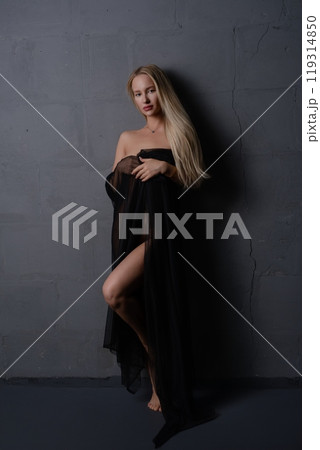 A woman draped in black fabric poses gracefully against a textured gray wall 119314850