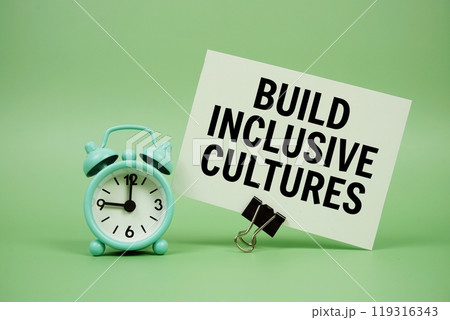 Build Inclusive Cultures text message on paper card with alarm clock on green background 119316343