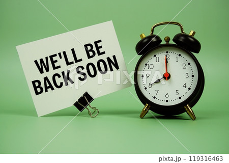 We'll Be Back Soon text message on paper card with alarm clcok on green background We'll Be Back Soon text message on paper card with alarm clcok on green background 119316463