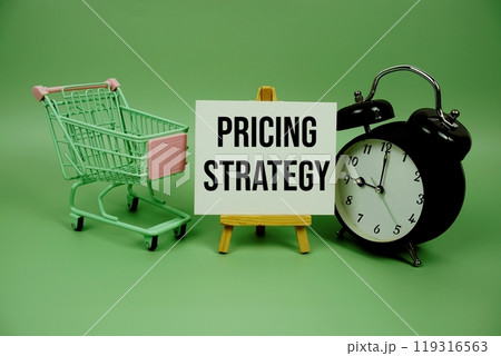 Pricing Strategy text message on paper card with alarm clcok and trolley shopping cart on green background 119316563