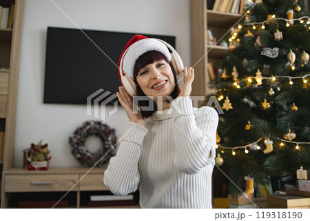 Young woman enjoying music with headphones near Christmas tree Young woman enjoying music with headphones near Christmas tree 119318190