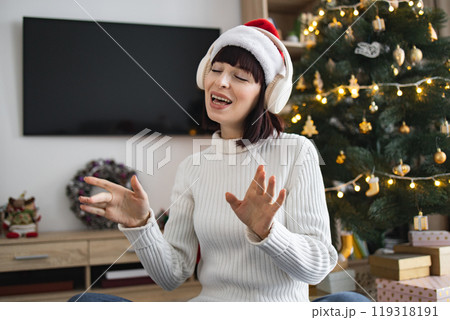 Woman enjoying Christmas music with headphones near decorated tree Woman enjoying Christmas music with headphones near decorated tree 119318191