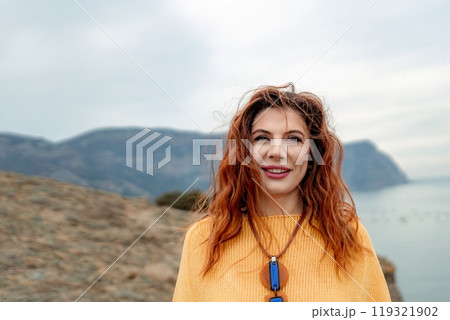 Portrait windswept hair happy woman against a backdrop of mountains and sea. Daylight illuminates the tranquil outdoor setting Portrait windswept hair happy woman against a backdrop of mountains and sea. Daylight illuminates the tranquil outdoor setting 119321902