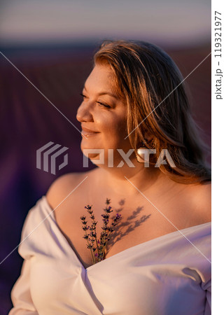 woman poses in lavender field at sunset. Happy woman in white dress holds lavender bouquet. Aromatherapy concept, lavender oil, photo session in lavender 119321977