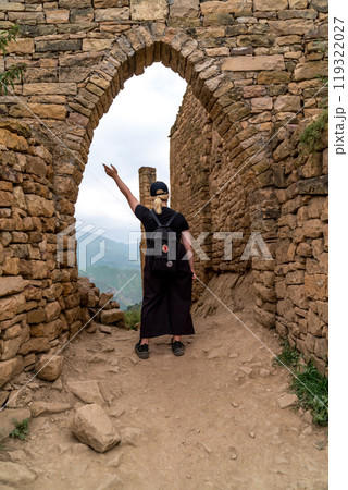 A woman is standing in front of a stone archway, pointing to the sky A woman is standing in front of a stone archway, pointing to the sky 119322027