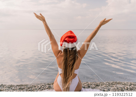 A woman wearing a red Santa hat is holding her hands together in a heart shape over the water. 119322512