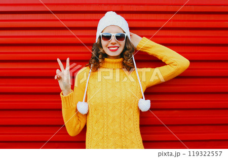 Fashion smiling young woman wearing colorful knitted yellow sweater over red background 119322557