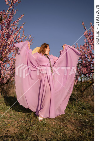 Woman blooming peach orchard. Against the backdrop of a picturesque peach orchard, a woman in a long pink dress and hat enjoys a peaceful walk in the park, surrounded by the beauty of nature. Woman blooming peach orchard. Against the backdrop of a picturesque peach orchard, a woman in a long pink dress and hat enjoys a peaceful walk in the park, surrounded by the beauty of nature. 119322678