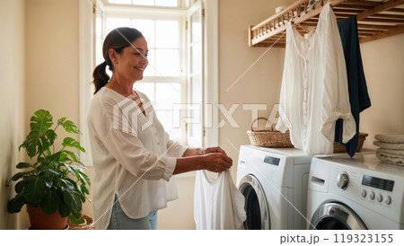 Woman taking care of laundry chores putting clothes in washing machine at home 119323155