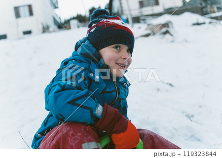 Little boy in warm clothes is sledding down a hill Little boy in warm clothes is sledding down a hill 119323844