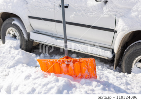 orange snow shovel sticking out from snowdrift in front of snow covered white SUV car 119324096