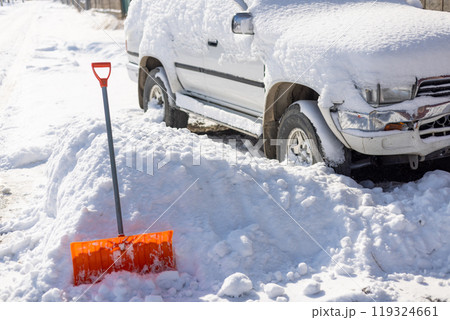 orange snow shovel sticking out from snowdrift in front of snow covered white SUV car 119324661