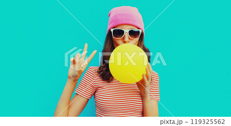 Fashion portrait of stylish cool young woman inflating chewing gum in pink hat on blue background Fashion portrait of stylish cool young woman inflating chewing gum in pink hat on blue background 119325562