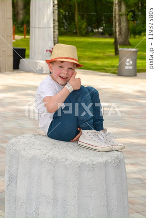 Smiling young blond boy sitting on bench at garden park on sunny day 119325805