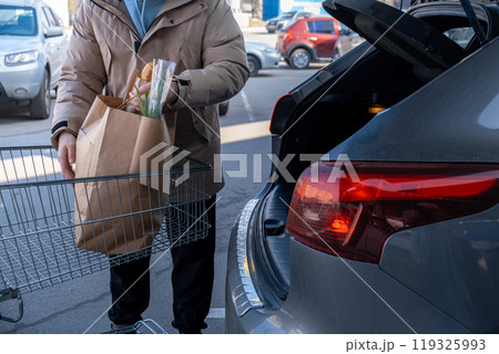 Man Loading Groceries into Car Trunk 119325993