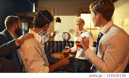 Friday mood. Men cheer as one successfully throws dart, enjoying their drinks and celebrating together. Friday mood. Men cheer as one successfully throws dart, enjoying their drinks and celebrating together. 119326130