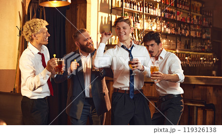 Group of colleagues playfully cheer as they playing games in bar, enjoying fun moment during their outing. 119326138