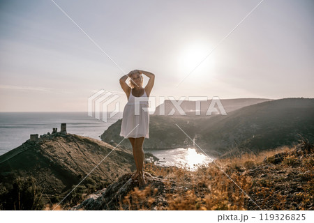 A blonde woman stands on a hill overlooking the ocean. She is wearing a white dress and she is enjoying the view. A blonde woman stands on a hill overlooking the ocean. She is wearing a white dress and she is enjoying the view. 119326825