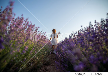 Lavender field girl. Back view happy girl in white dress with a scythe runs through a lilac field of lavender. Aromatherapy travel Lavender field girl. Back view happy girl in white dress with a scythe runs through a lilac field of lavender. Aromatherapy travel 119326836