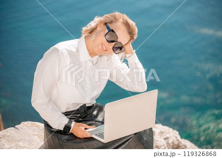 Business woman on nature in white shirt and black skirt. She works with an iPad in the open air with a beautiful view of the sea. The concept of remote work. Business woman on nature in white shirt and black skirt. She works with an iPad in the open air with a beautiful view of the sea. The concept of remote work. 119326868