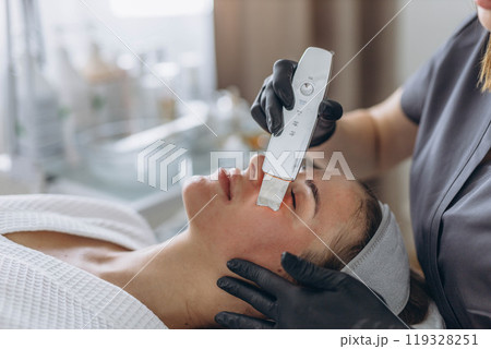 Cosmetologist making facial treatment with ultrasonic spatula to young woman. Cosmetologist making facial treatment with ultrasonic spatula to young woman. 119328251