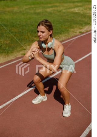 An active woman performing squats on a track while wearing stylish sportswear for fitness 119329525
