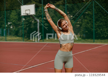 An Active Young Woman Engaging in Stretching Exercises on a Tennis Court to Enhance Flexibility An Active Young Woman Engaging in Stretching Exercises on a Tennis Court to Enhance Flexibility 119329544