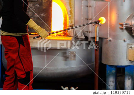 Close-up glassblowing process tube tool with molten glass shaped inside refractory furnace in industrial craft workshop. Handmade blowing glassware design production manufacture Europe Close-up glassblowing process tube tool with molten glass shaped inside refractory furnace in industrial craft workshop. Handmade blowing glassware design production manufacture Europe 119329715