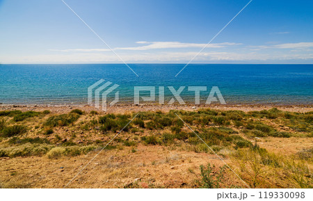 large open water surface with far snowcapped mountain range on the horizon and wild rocky beach in at sunny day 119330098