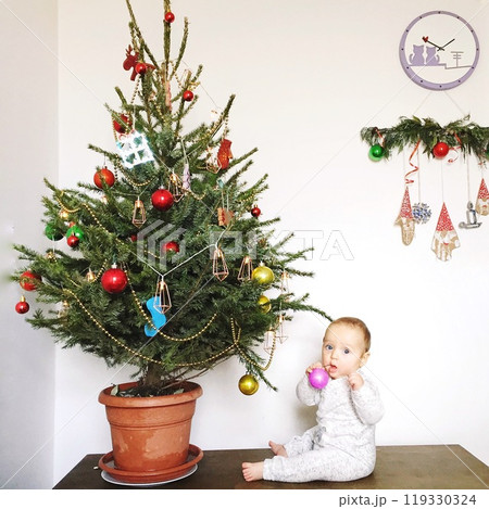 Little baby with a live Christmas tree with background of white wall with Christmas decorations 119330324