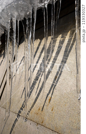Beautiful spring icicles dripping down from snow covered roof along metal wall. Vertical format. 119330327