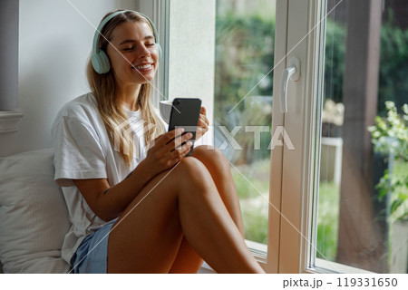 Relaxing Moment A Young Woman Featuring Enjoyment of Music While Resting By The Window 119331650