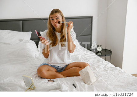 A young woman skillfully applying her makeup in a comfortably cozy bedroom setting A young woman skillfully applying her makeup in a comfortably cozy bedroom setting 119331724