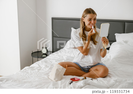 Morning Routine A Woman Applying Her Makeup While Comfortably Sitting on Her Bed, Relaxed 119331734