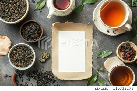 Assorted tea leaves, cups of tea, and brewing accessories surrounding a blank card on dark background, perfect for customizable design 119332173