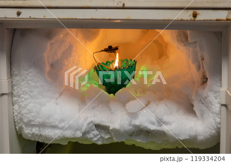 The freezer compartment of the refrigerator is covered with pieces of ice in which there is a burning candle The freezer compartment of the refrigerator is covered with pieces of ice in which there is a burning candle 119334204