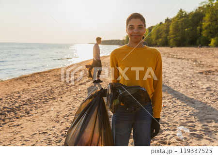 Earth day. Volunteers activists team collects garbage cleaning of beach coastal zone. Woman mans puts plastic trash in garbage bag on ocean shore. Environmental conservation coastal zone cleaning Earth day. Volunteers activists team collects garbage cleaning of beach coastal zone. Woman mans puts plastic trash in garbage bag on ocean shore. Environmental conservation coastal zone cleaning 119337525