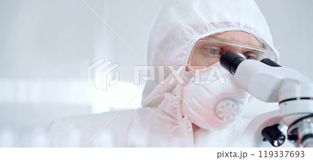 Professional scientist in protective gear is using microscope in a laboratory setting and alarm red light. Science and medicine concepts Professional scientist in protective gear is using microscope in a laboratory setting and alarm red light. Science and medicine concepts 119337693