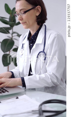 Doctor woman is working with laptop computer at the glass table in clinic. Physician is typing medical information or giving advices online. Medicine and pharmacy Doctor woman is working with laptop computer at the glass table in clinic. Physician is typing medical information or giving advices online. Medicine and pharmacy 119337707