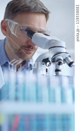 Man scientist with protective glasses and gloves is using microscope in laboratory, vertical portrait of researcher. Microbiology science concept Man scientist with protective glasses and gloves is using microscope in laboratory, vertical portrait of researcher. Microbiology science concept 119338081