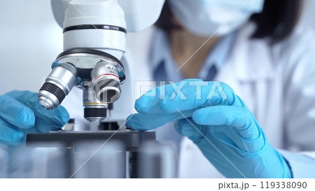 Scientist using microscope in laboratory. Close-up of a researcher's hands adjusting a modern microscope in a lab setting 119338090