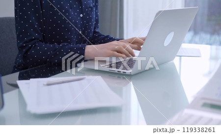 A female accountant or businesswoman with blue dotted blousy is typing on laptop computer on glass desk in the office. Business people concept A female accountant or businesswoman with blue dotted blousy is typing on laptop computer on glass desk in the office. Business people concept 119338261