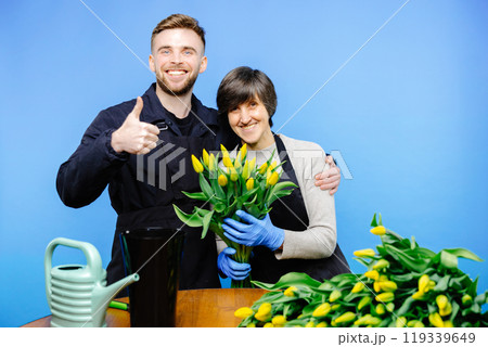 Flower shop. A young guy helps an older woman florist take care of flowers in a flower studio Flower shop. A young guy helps an older woman florist take care of flowers in a flower studio 119339649