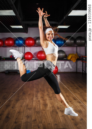 Woman performing a joyful energetic dance leap in a fitness studio with exercise balls 119339668