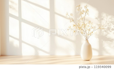 A serene setting featuring a simple white vase with delicate flowers, illuminated by soft sunlight filtering through a window, casting gentle shadows on a wooden surface. 119340099